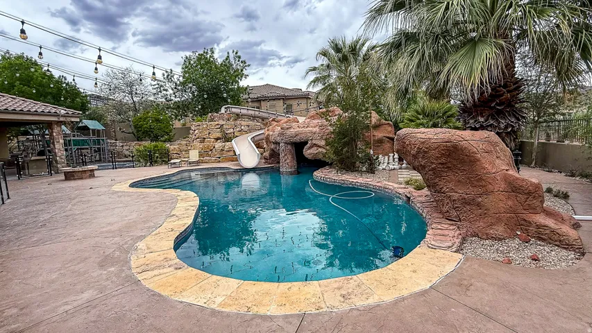 Freeform swimming pool with a rock grotto, integrated waterslide, and stamped concrete decking