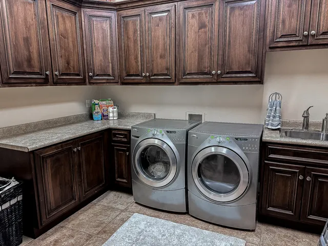 Utility room featuring extensive wood cabinetry, L-shaped countertop, ceramic tile flooring, and an integrated sink with faucet
