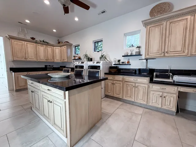Central island with dark countertop, extensive cabinetry with ornate detailing, recessed lighting, and light tile flooring