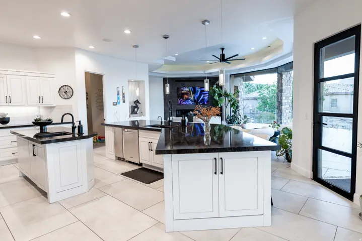 Kitchen featuring light-toned tile flooring, white cabinetry, dark countertops, and dual islands with integrated sinks
