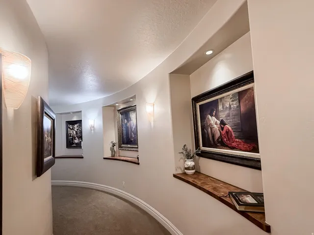Curved hallway featuring recessed art niches with wood-finish shelving, wall sconces, and recessed lighting