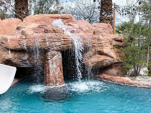 Pool with rock waterfall feature, integrated water slide, grotto, and string lighting