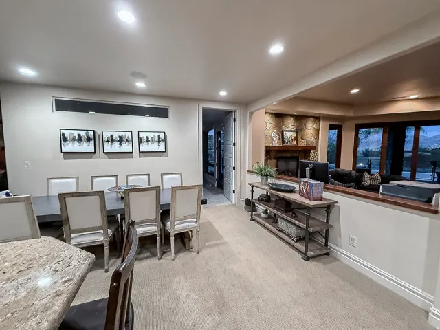 Open-concept living area with a stone fireplace, wood mantel, and large windows