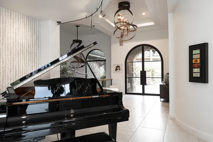 Arched double entry doors, a coffered ceiling with a tiered chandelier, and tile flooring