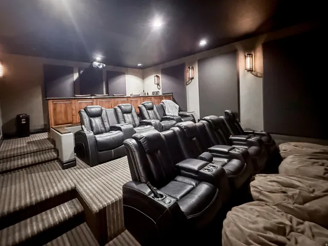 Dedicated home theater with multi-tiered seating, integrated wall sconces, and overhead recessed lighting