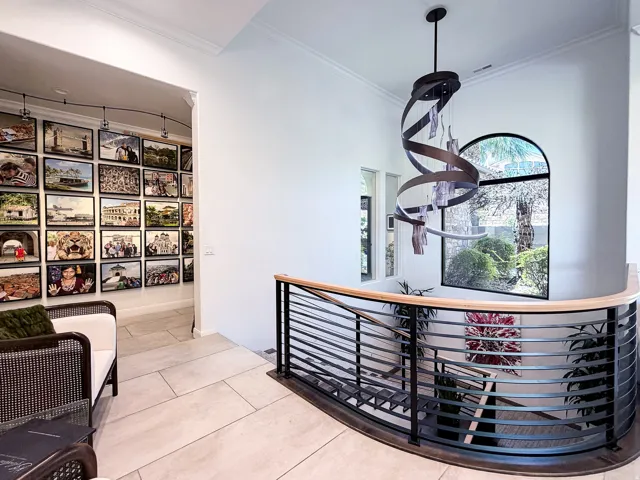 Curved metal stair railing with a wood-finish top rail, arched window, contemporary pendant light fixture, and tile flooring