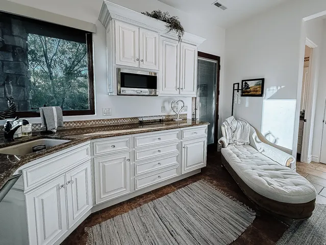 White shaker-style cabinetry with crown molding, granite countertops, an undermount sink with a gooseneck faucet, a built-in microwave, and tile flooring