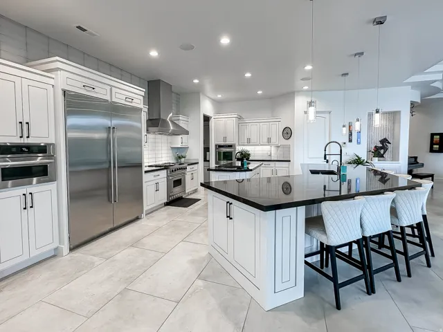 Gourmet kitchen featuring a large central island, stainless steel appliances, white cabinetry, and light-toned tile flooring
