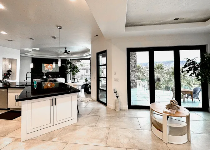 Open concept living area with large format tile flooring, a kitchen island featuring a black countertop and white cabinetry, recessed lighting, and expansive glass doors leading to an outdoor area