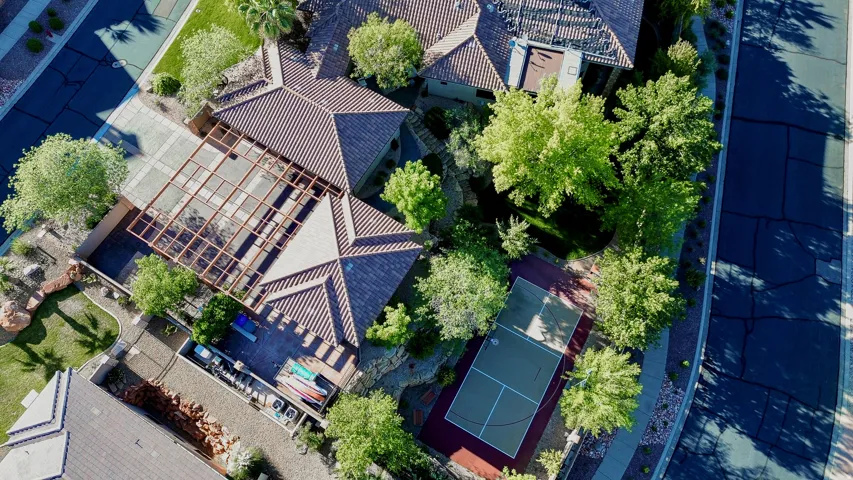 Terracotta tile roofing, covered patio with open-frame trellis, outdoor sport court, and mature landscaping