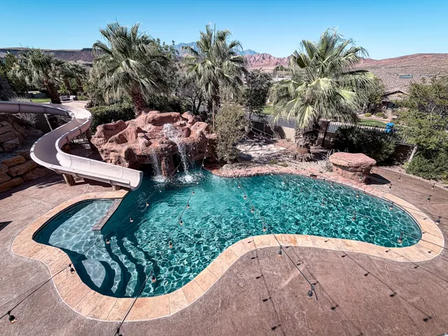 Freeform swimming pool with rock waterfall feature, integrated water slide, and stone-look decking