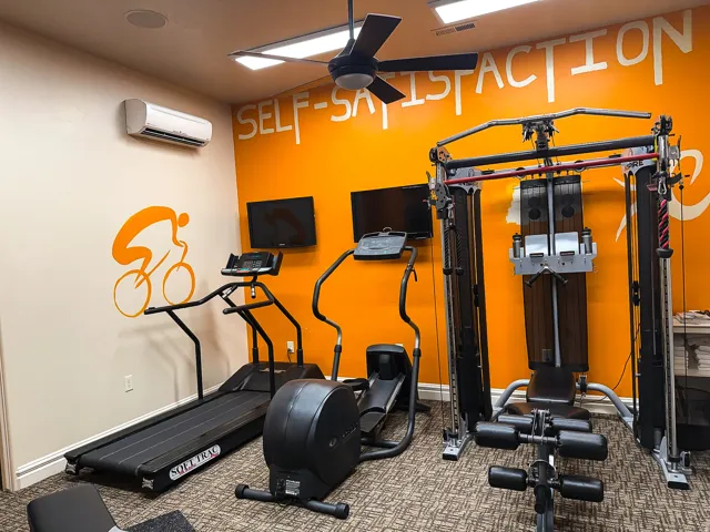 Dedicated fitness space featuring patterned carpet flooring, ceiling fan, and wall-mounted climate control unit