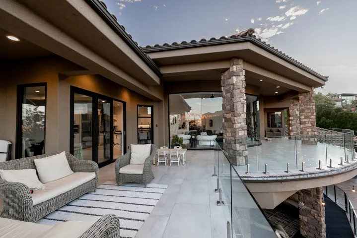 Expansive stone-clad columns, durable stucco exterior, large format tile patio, glass panel railings, and sliding glass doors