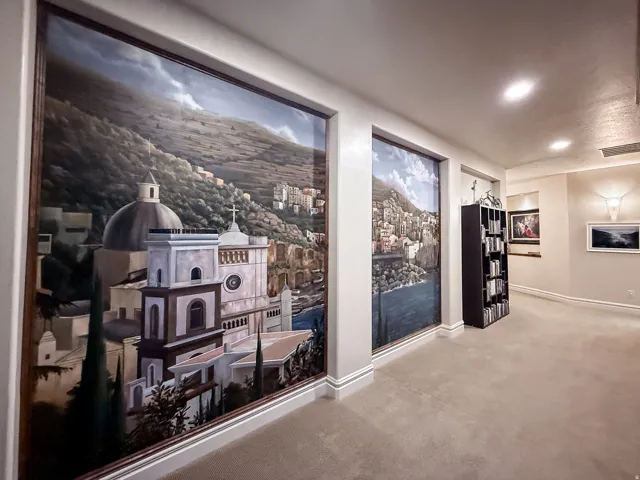 Hallway featuring large-format wall murals depicting Mediterranean architectural landmarks and coastal landscapes, polished concrete flooring, recessed ceiling lighting, and built-in shelving with display space