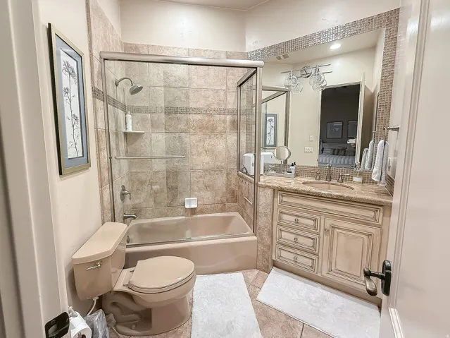Tiled shower and bathtub combination with a glass enclosure, single vanity with a stone countertop, and a mosaic tile backsplash