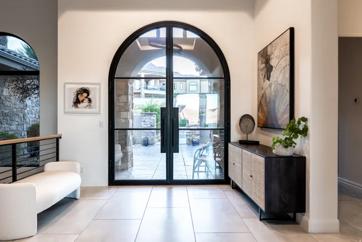 Arched iron and glass entry doors, light-toned tile flooring, and a stone exterior feature