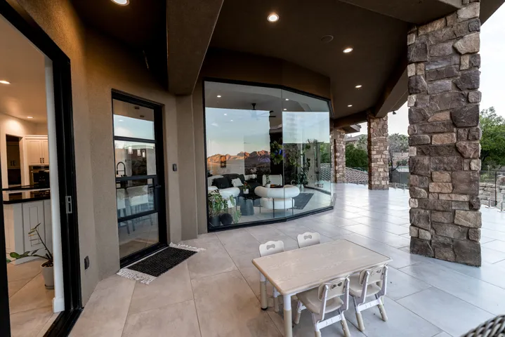 Expansive outdoor patio featuring stone columns, recessed lighting, and a full glass wall