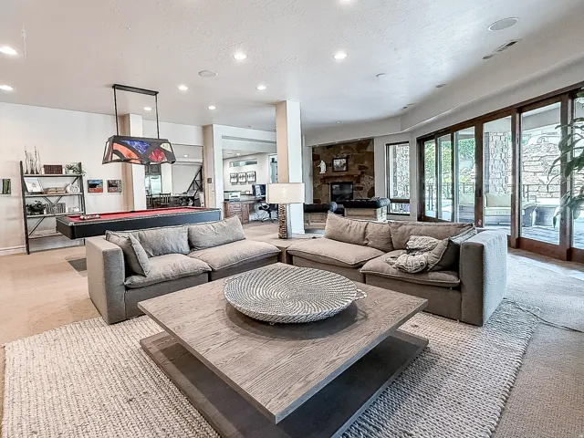 Recessed ceiling lighting, stone-clad fireplace, built-in shelving, wood-framed sliding glass doors, and a built-in pool table