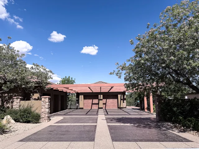 Exposed aggregate driveway with dark paver accents, shaded by a wooden pergola with a red finish