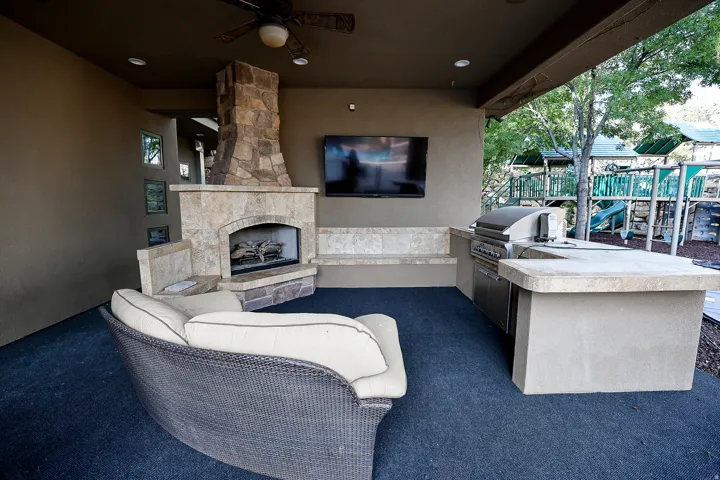 Covered outdoor patio featuring a stone-clad fireplace, integrated outdoor kitchen, built-in shelving, a ceiling fan, and recessed lighting