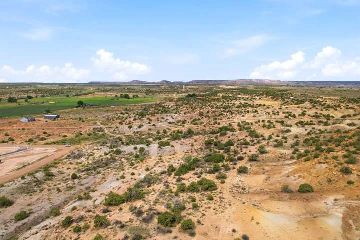 Expansive rural landscape featuring a mix of arid terrain and cultivated fields, with distant hills and scattered structures