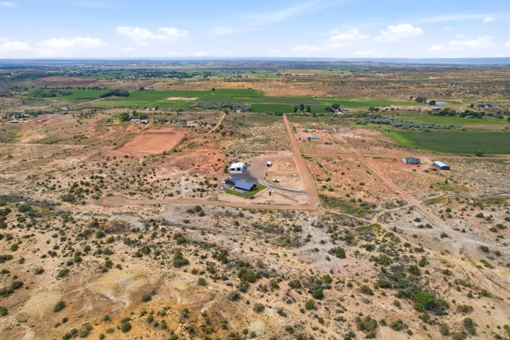 Expansive property featuring a residence with solar panels, multiple outbuildings, and a surrounding arid landscape