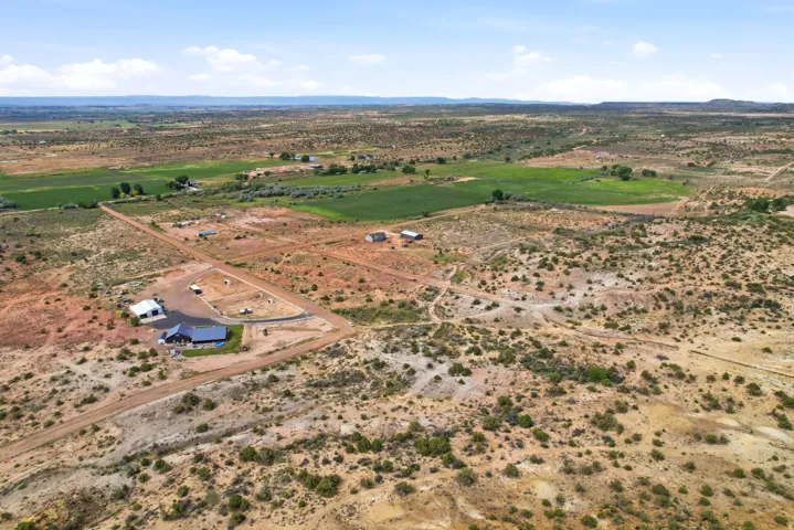 Rural landscape featuring a residential structure with a dark roof, an additional barn-style building, and surrounding dirt roads