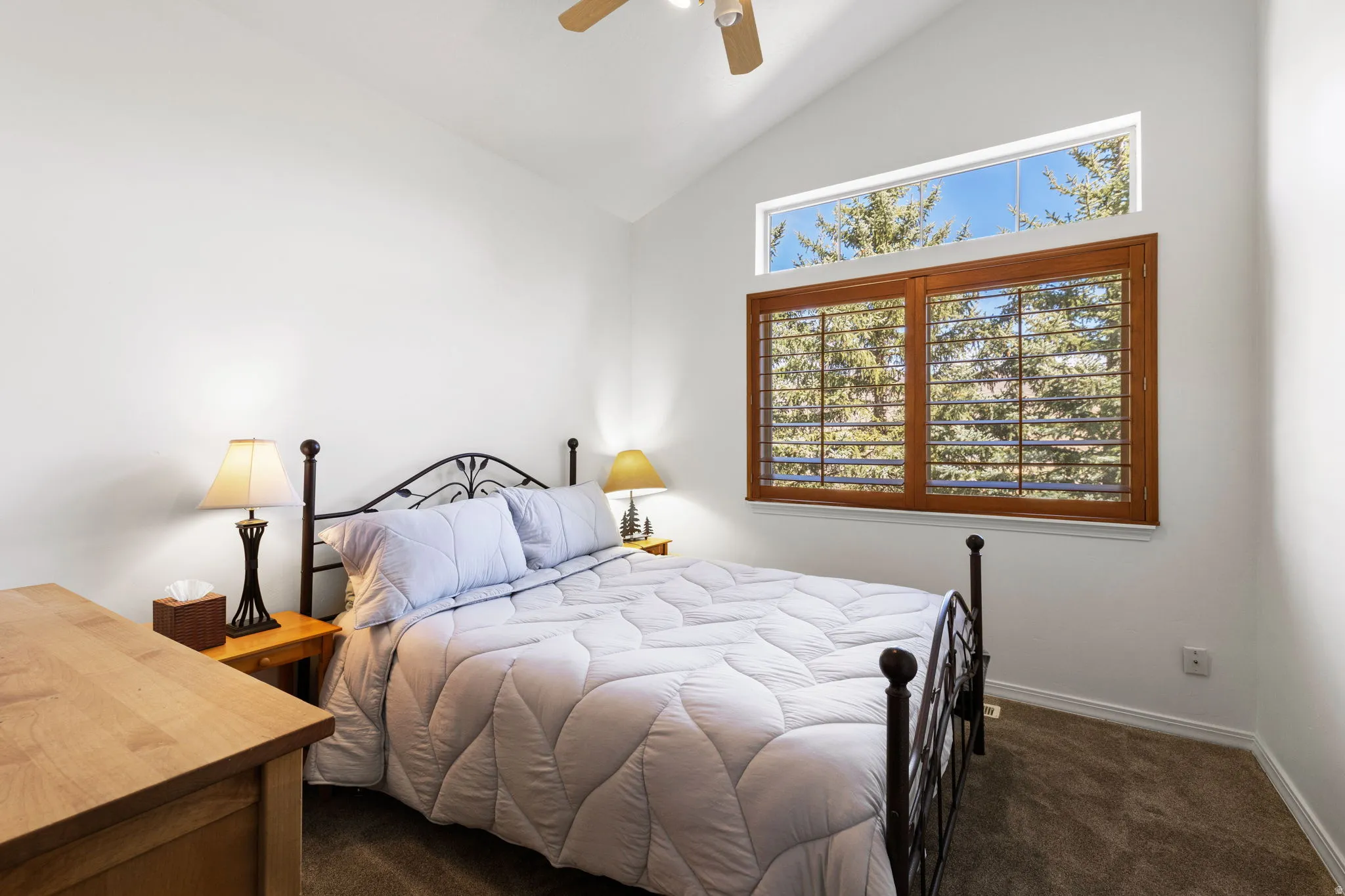Vaulted ceiling bedroom with a wood-framed window and upper transom, featuring plantation shutters