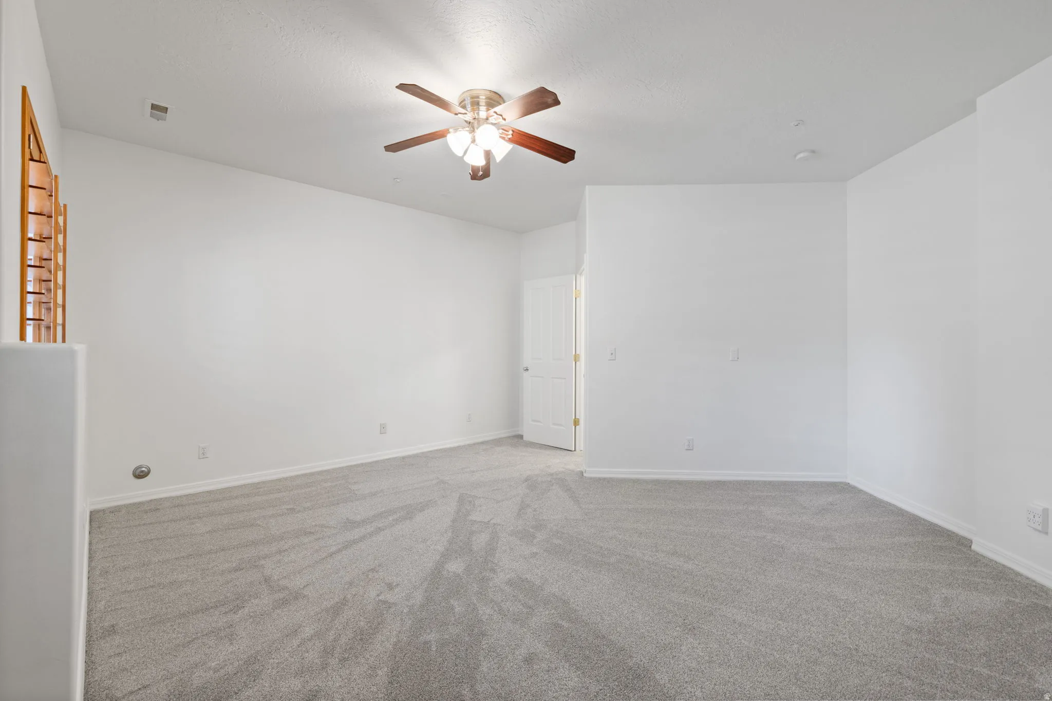 Spacious room with light gray carpeting, neutral white walls, a ceiling fan with light fixture, and a white paneled door
