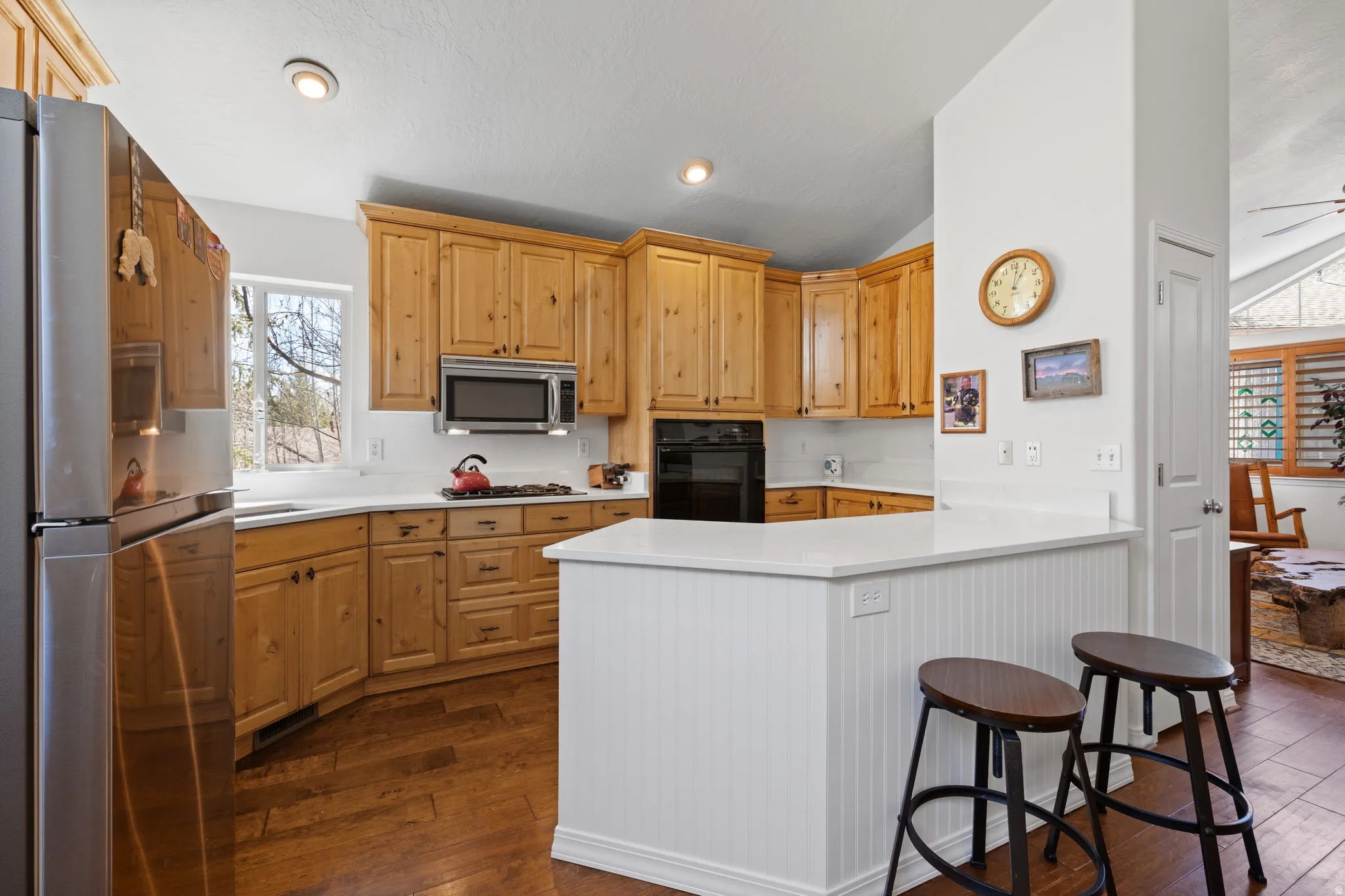 Kitchen featuring wood-finish flooring, light wood cabinetry, white countertops, stainless steel appliances, and a breakfast bar with beadboard paneling