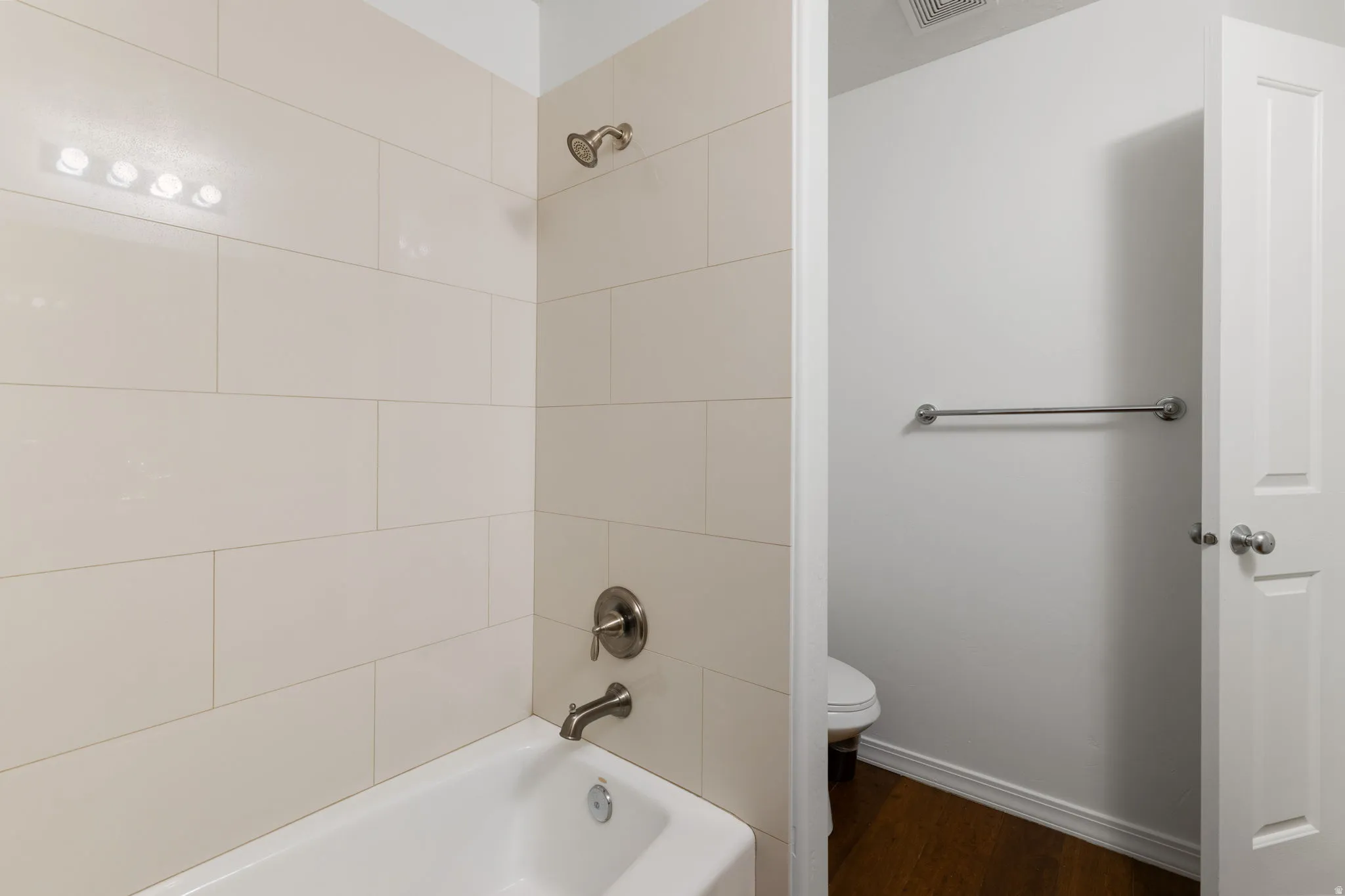 Bathtub with subway tile surround, brushed nickel fixtures, and a four-bulb vanity light
