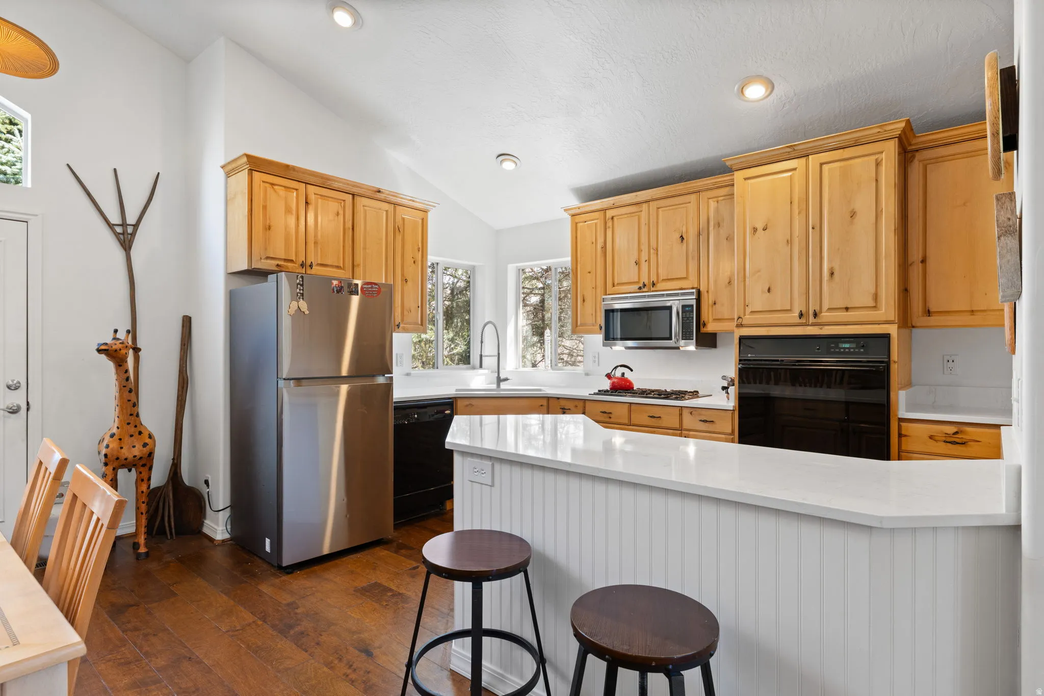 Kitchen featuring natural wood cabinetry, stainless steel appliances, white countertops, and wood-finish flooring
