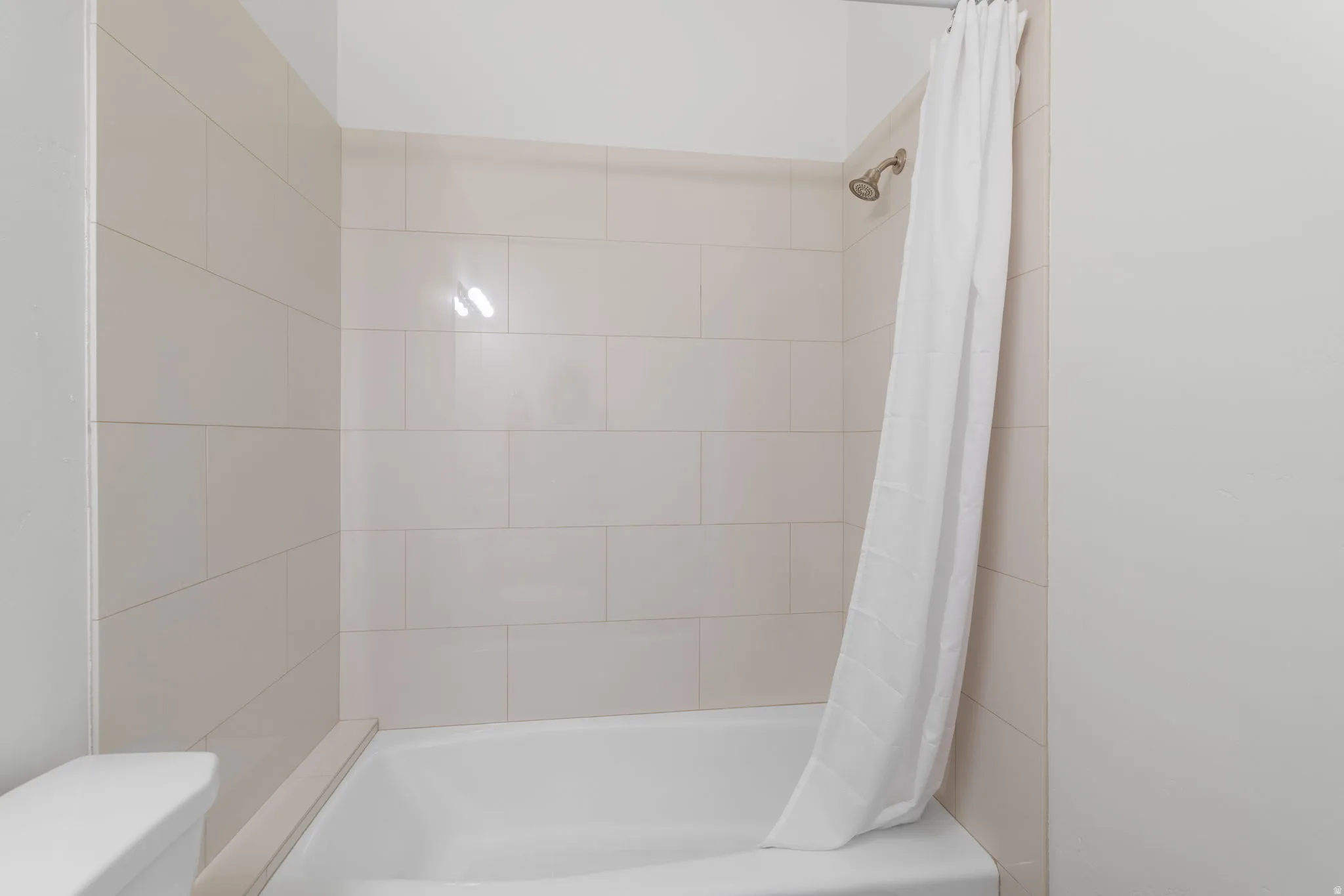 Bathtub and shower combination featuring neutral-toned subway tile surround and a brushed nickel shower head