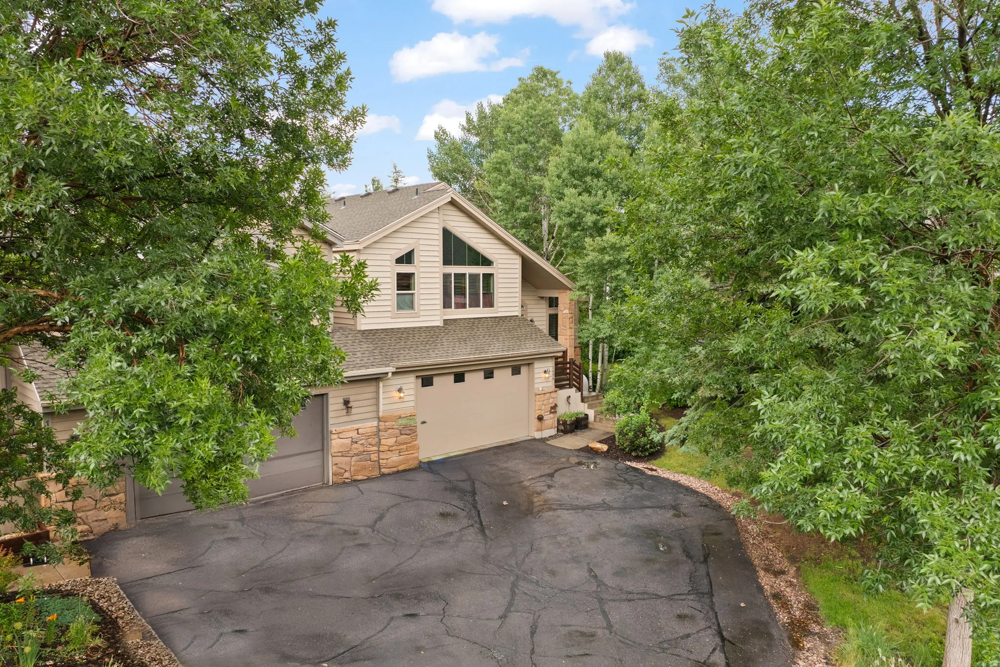 Contemporary exterior featuring a gabled roofline, multiple garage doors, stone accents, and a large triangular window array