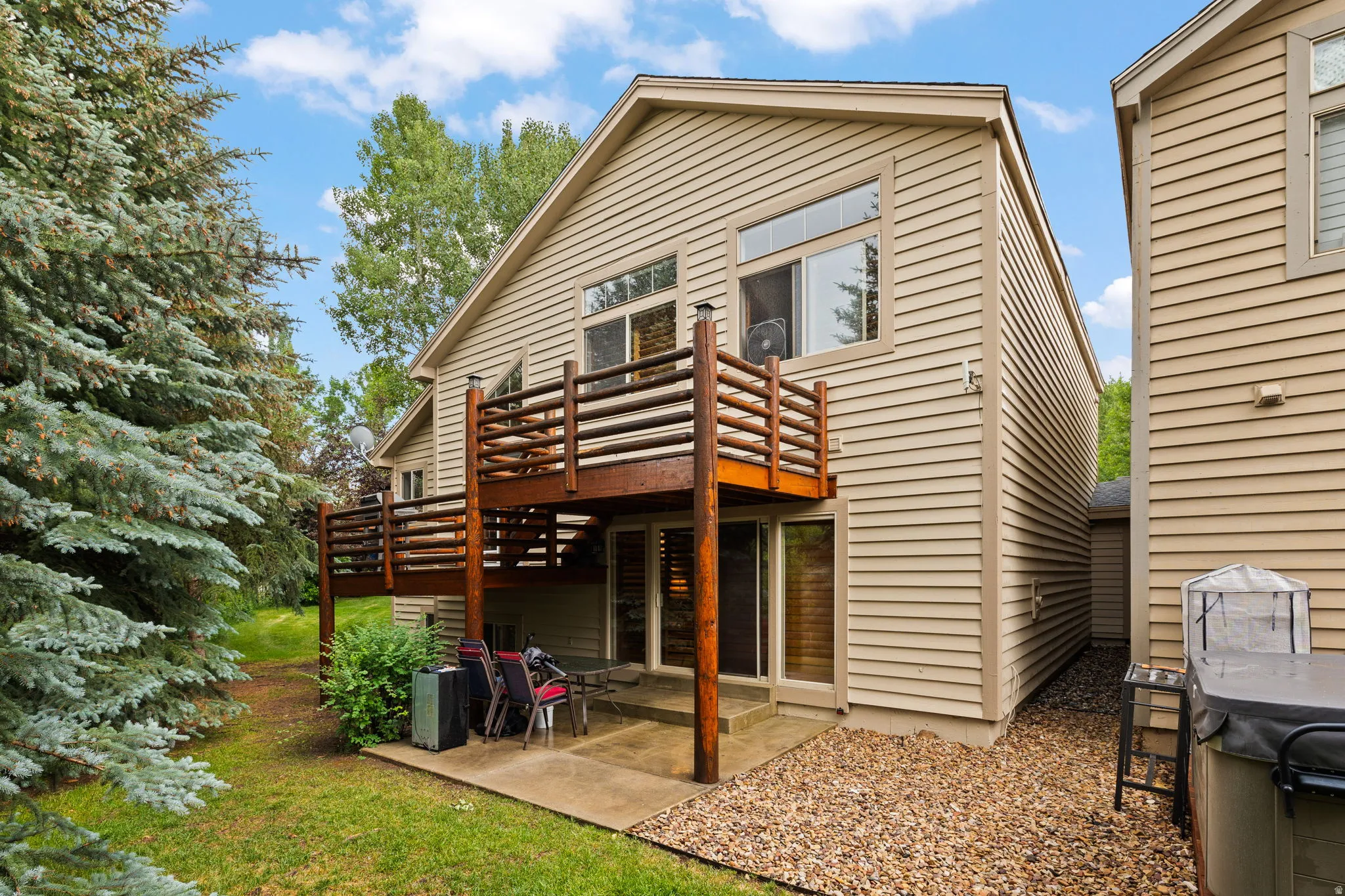 Rear exterior featuring a spacious wood-deck balcony, lower-level patio, and extensive natural landscaping