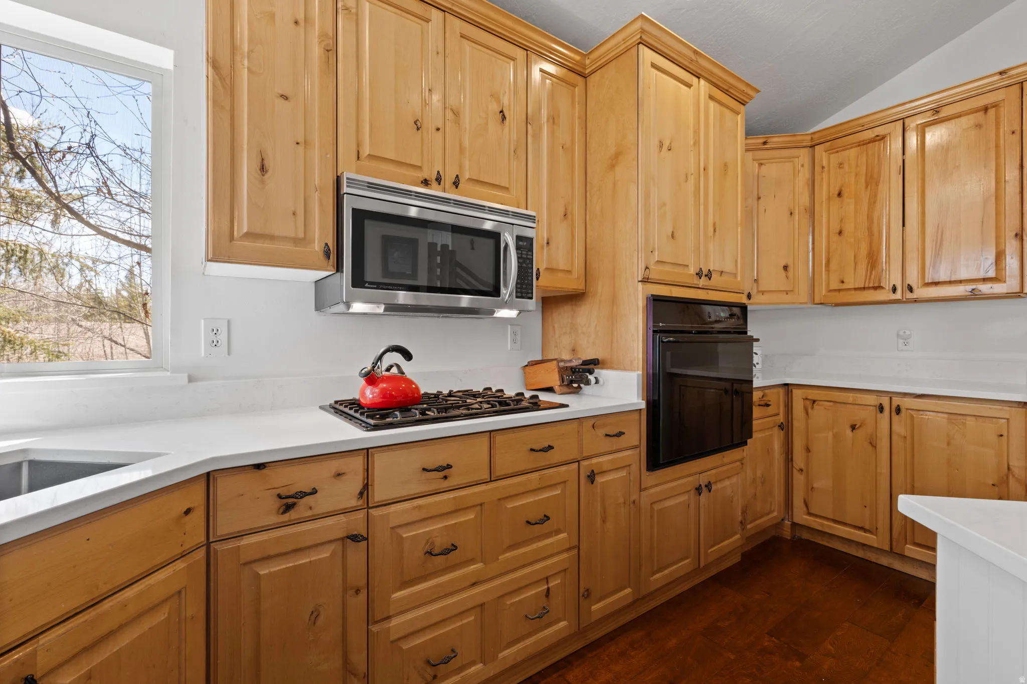 Kitchen featuring light wood cabinetry, white countertops, built-in oven, stainless steel microwave, and a gas cooktop