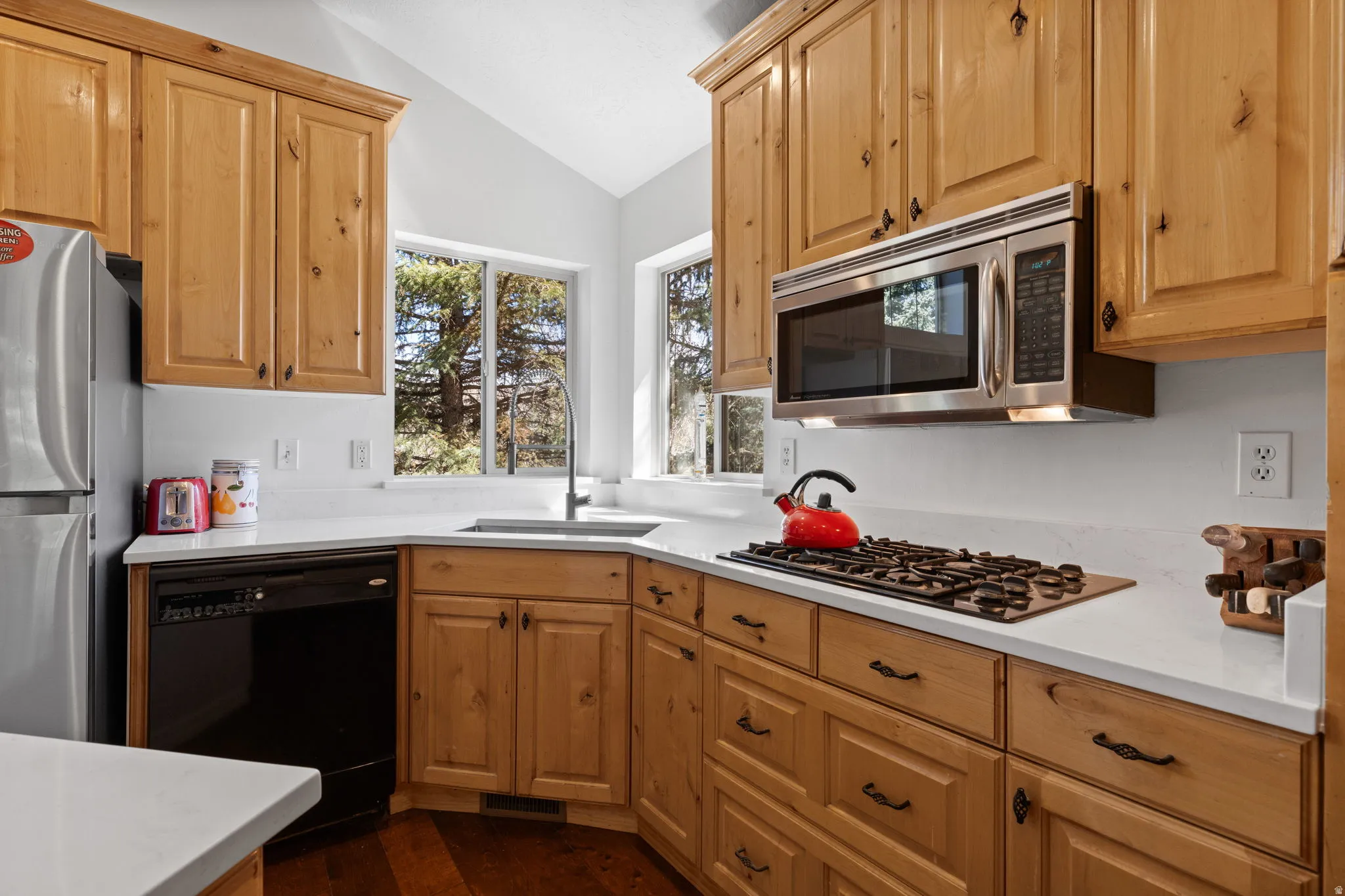 Kitchen featuring wood cabinetry, light-toned countertops, a stainless steel microwave, a built-in gas cooktop, and a stainless steel refrigerator