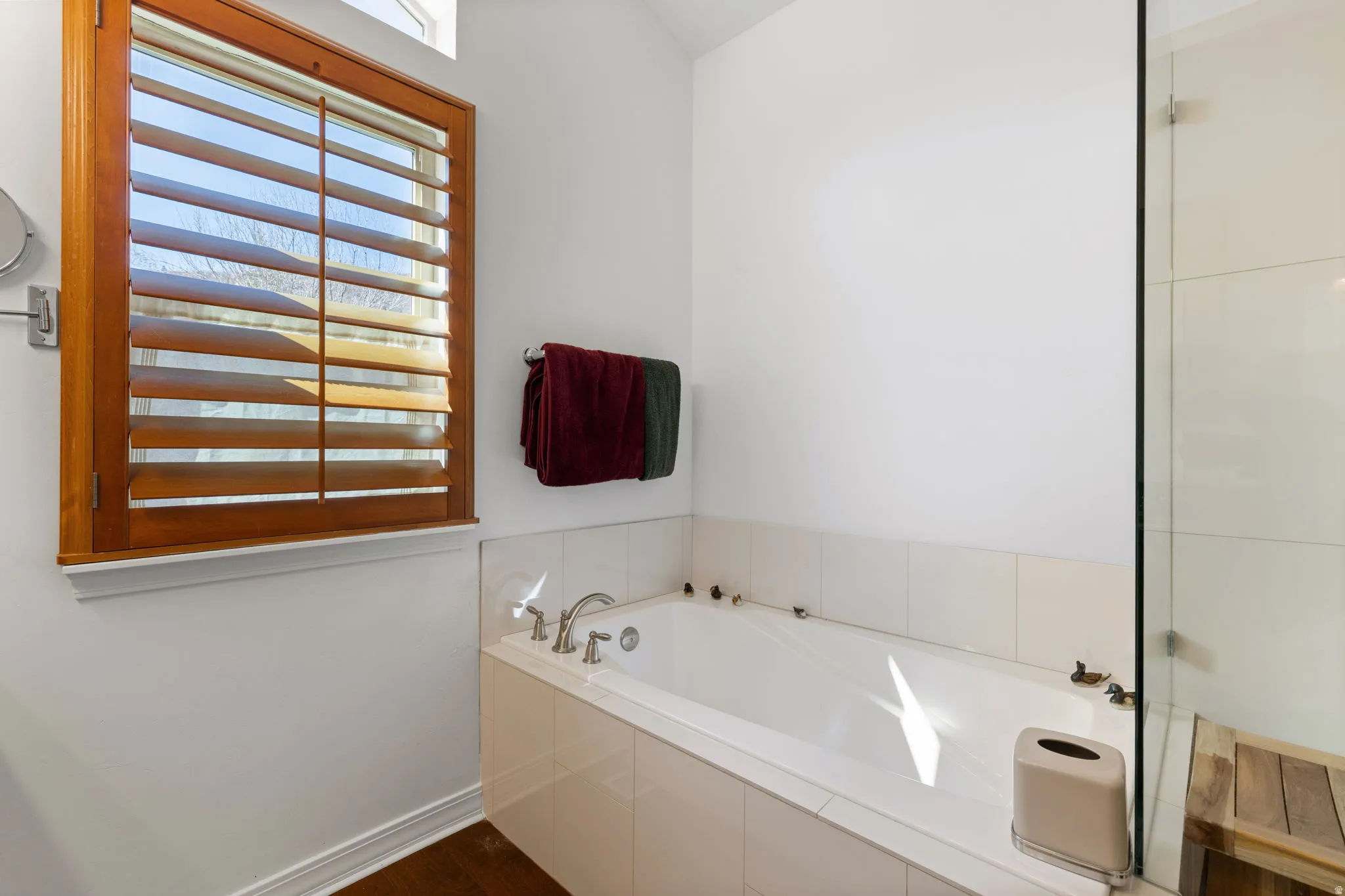 Built-in soaking tub with deck-mounted fixtures, surrounded by white tile and a clear glass shower enclosure