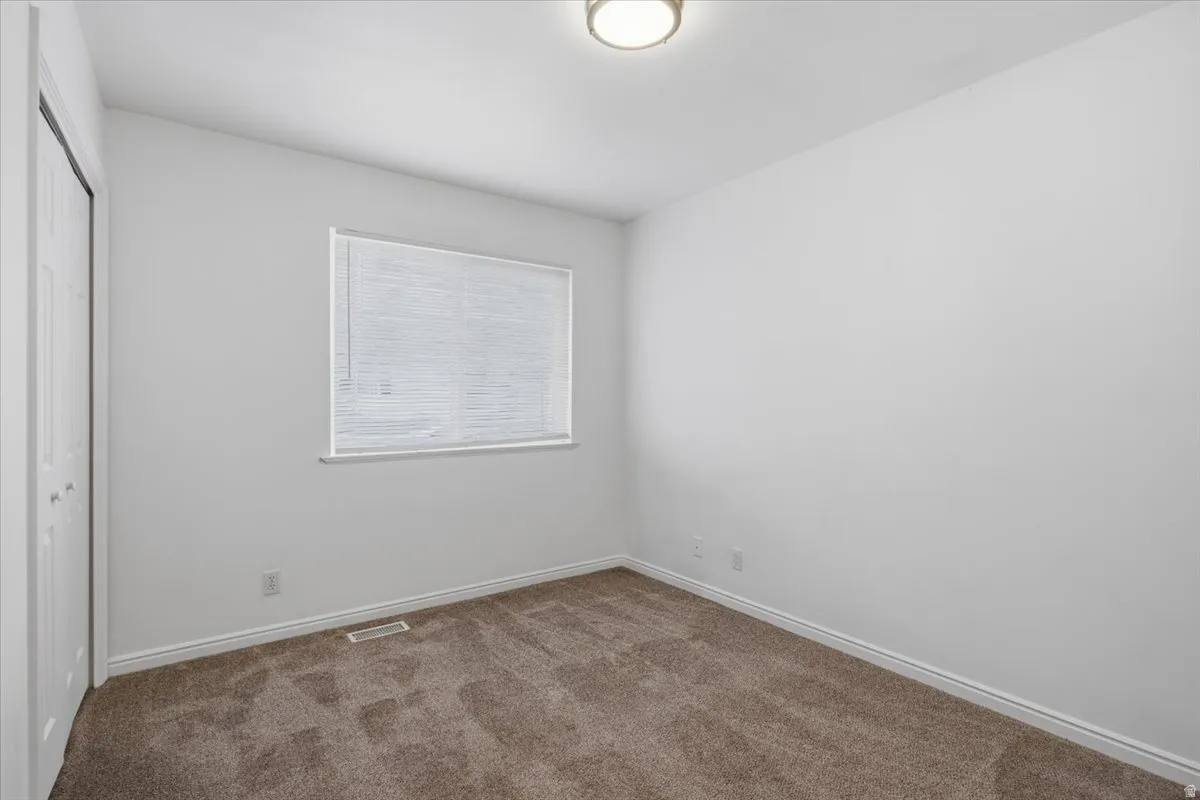 Neutral wall color, carpet flooring, window with blinds, bi-fold closet doors, and flush mount lighting