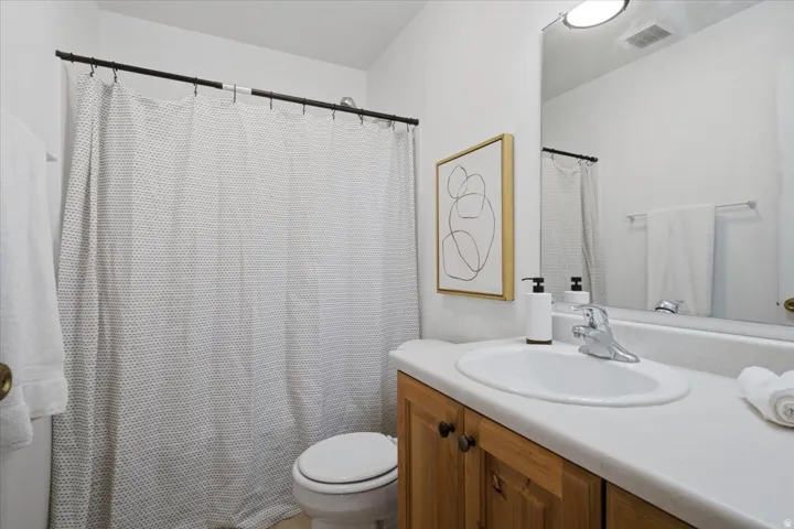 Bathroom featuring a wood-finish vanity with a white countertop and an integrated sink, a toilet, a shower/tub combination with a shower rod, and a wall-mounted mirror