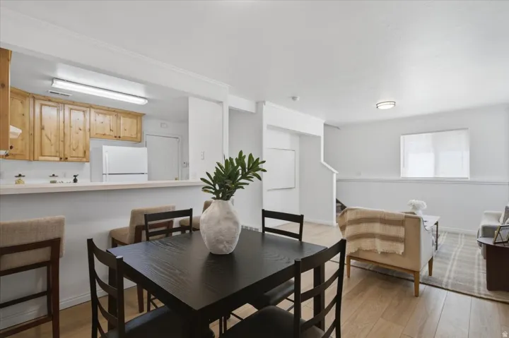 Open-concept living area with wood-finish flooring, a kitchen featuring wood cabinetry and white appliances, and a breakfast bar with a light countertop