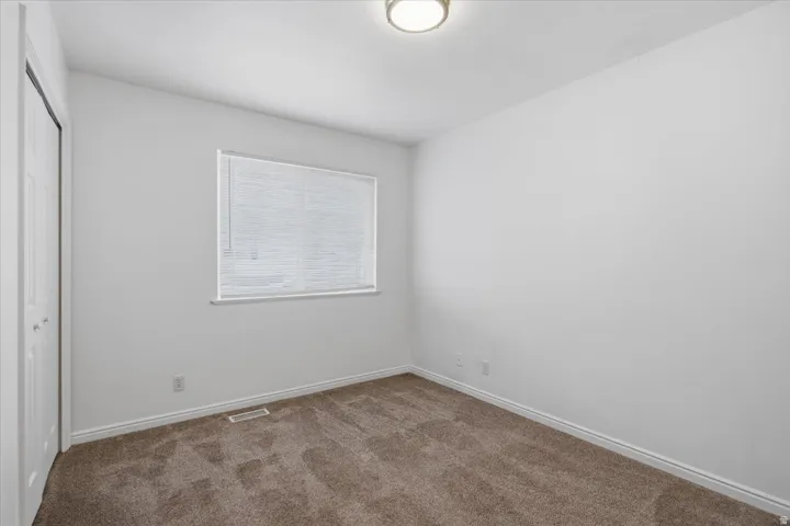 Neutral wall color, carpet flooring, window with blinds, bi-fold closet doors, and flush mount lighting