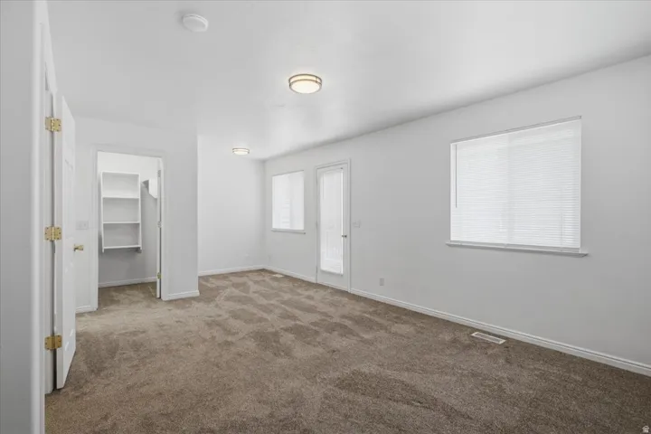Spacious room featuring neutral carpeting, white walls, multiple windows with blinds, a walk-in closet with built-in shelving, and flush-mount ceiling lights
