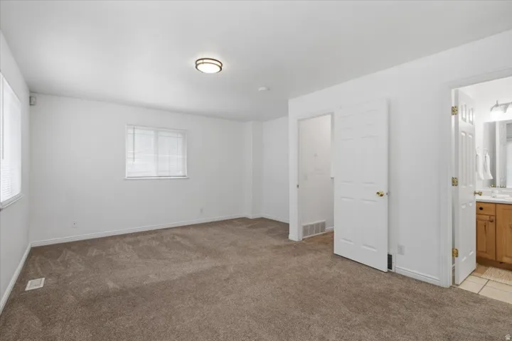Recessed lighting fixture, plush carpet flooring, multiple windows with blinds, white paneled doors, and an attached bathroom with a wood-finish vanity