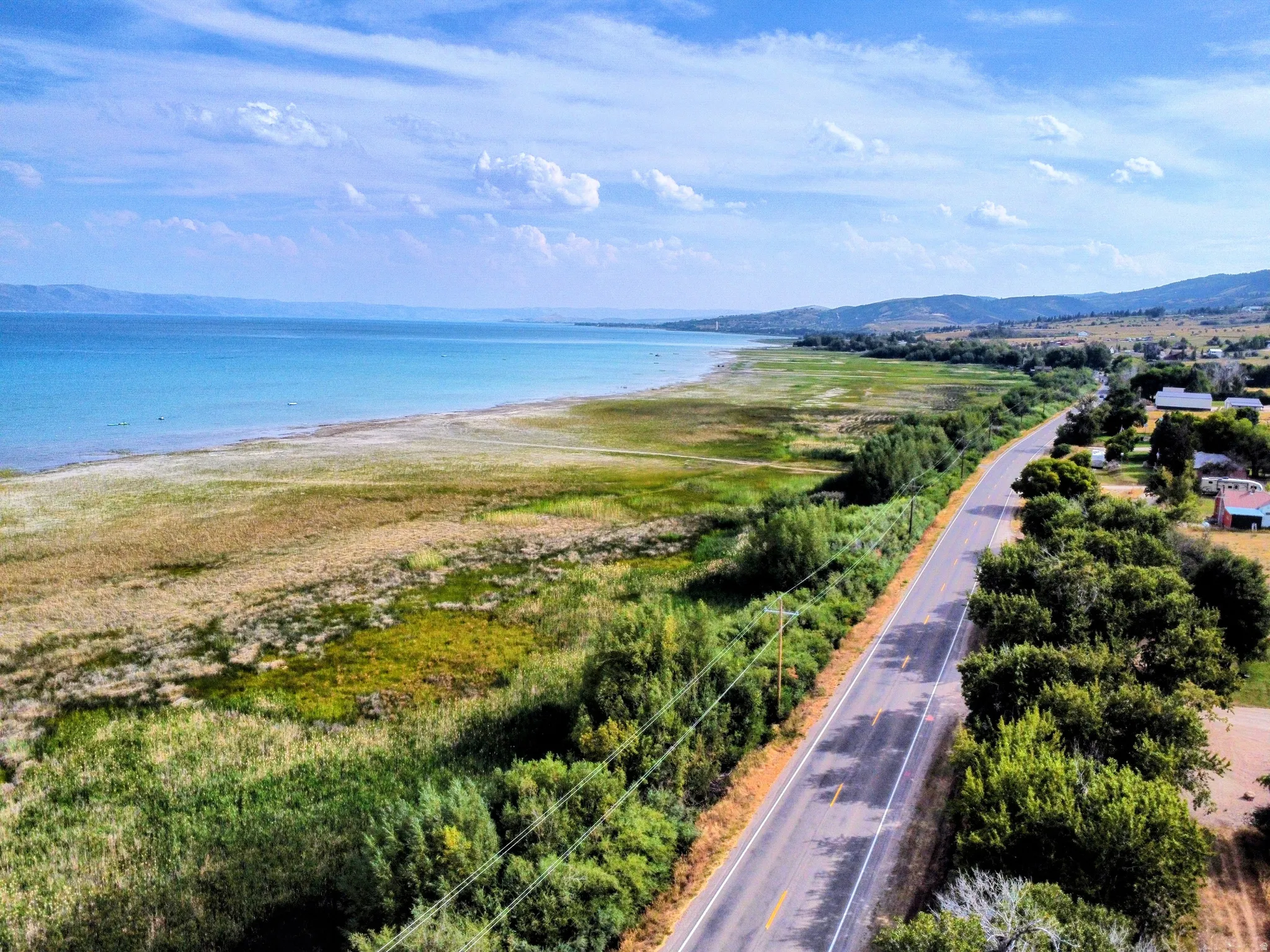 Expansive waterfront acreage with natural vegetation, bordered by a paved roadway and distant mountainous terrain