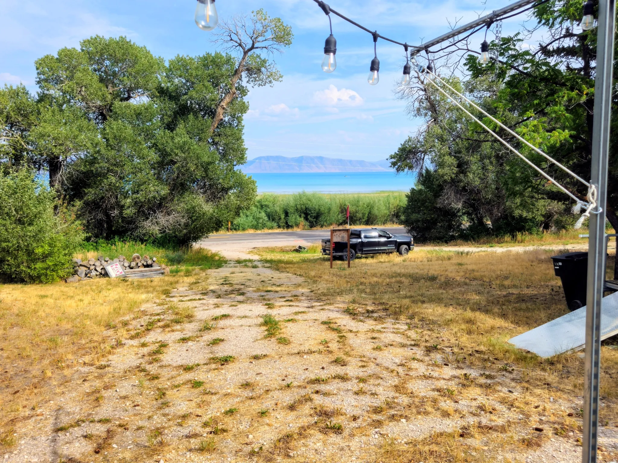 String lighting fixture with exposed bulbs, mature trees, and distant body of water