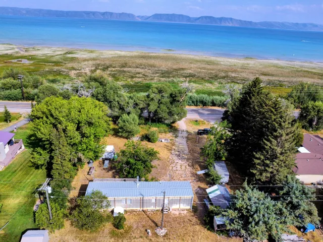 Waterfront property with mountain scenery, featuring a single-story structure with a metal roof and mature trees on the lot