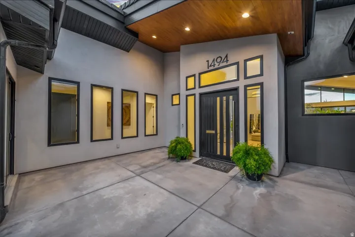 Modern exterior featuring a dark double entry door, an array of rectangular windows with dark trim, a wood-finish soffit, and concrete hardscaping
