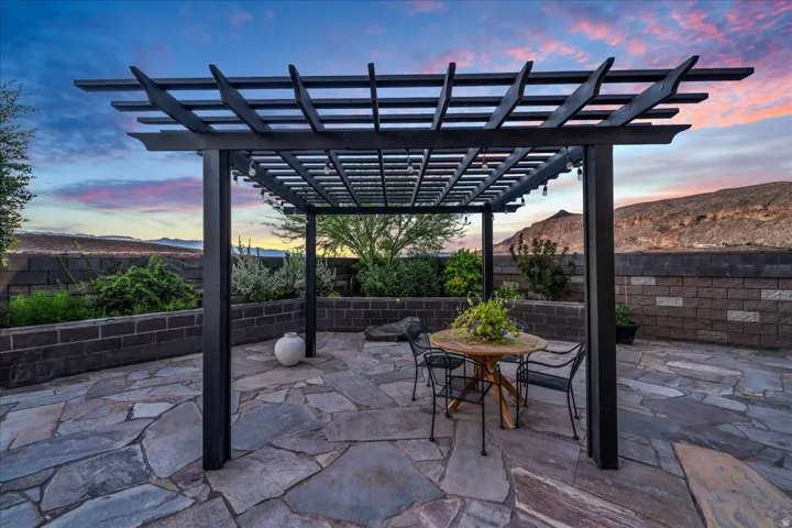 Expansive flagstone patio featuring a black pergola, integrated lighting, and tiered retaining walls
