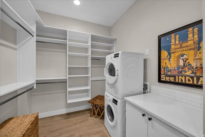 Integrated laundry appliances with a countertop, white subway tile backsplash, custom white shelving, hanging rods, and wood-finish flooring